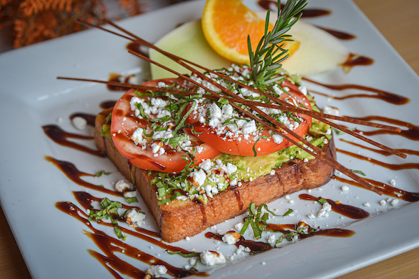Inside the Creative Process at Hash House A Go Go: How Our Unique Food Creations Come to Life 3 Avocado toast topped with tomato slices, feta cheese, herbs, and balsamic drizzle at Hash House A Go Go in Las Vegas.