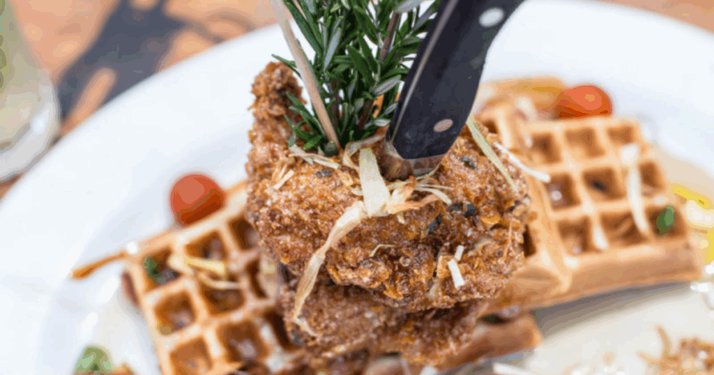 The Secret Behind the Best Sage Fried Chicken & Waffles in Las Vegas 9 Crispy sage fried chicken stacked on golden waffles at Hash House A Go Go in Las Vegas, garnished with rosemary and fried leeks