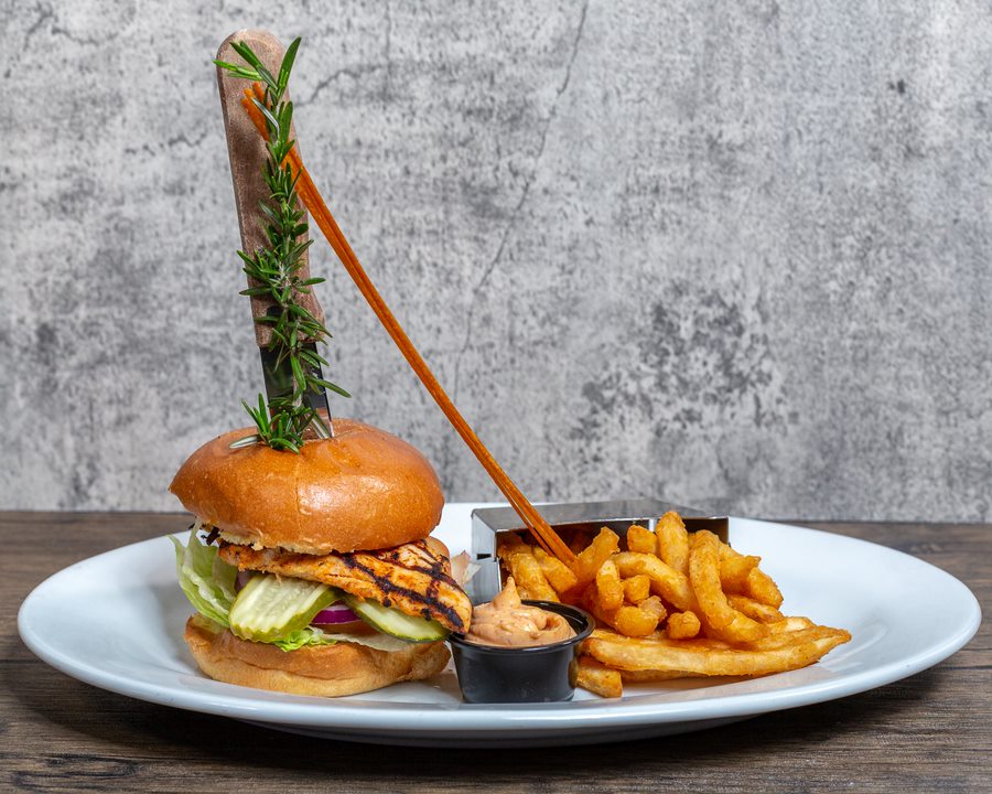 Celebrating Las Vegas Culture Through Dining at Hash House A Go Go 1 Grilled spicy chicken sandwich with lettuce, tomato, and onion on a brioche bun, served with curly fries and dipping sauce at Hash House A Go Go—highlighting Las Vegas dining culture through bold flavor and oversized presentation.