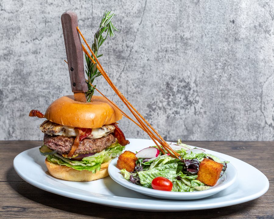 Plated burger and salad featuring fresh ingredients like lettuce, bacon, egg, cheese, radish, tomato, and house-made dressing at Hash House A Go Go.