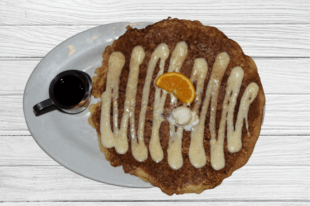 The Ultimate Guide to Twisted Farm Food: Why Hash House A Go Go Is a Must-Try in Las Vegas 1 Cinnamon roll pancake drizzled with icing and served with syrup at Hash House A Go Go in Las Vegas—a comfort food favorite for breakfast or brunch.